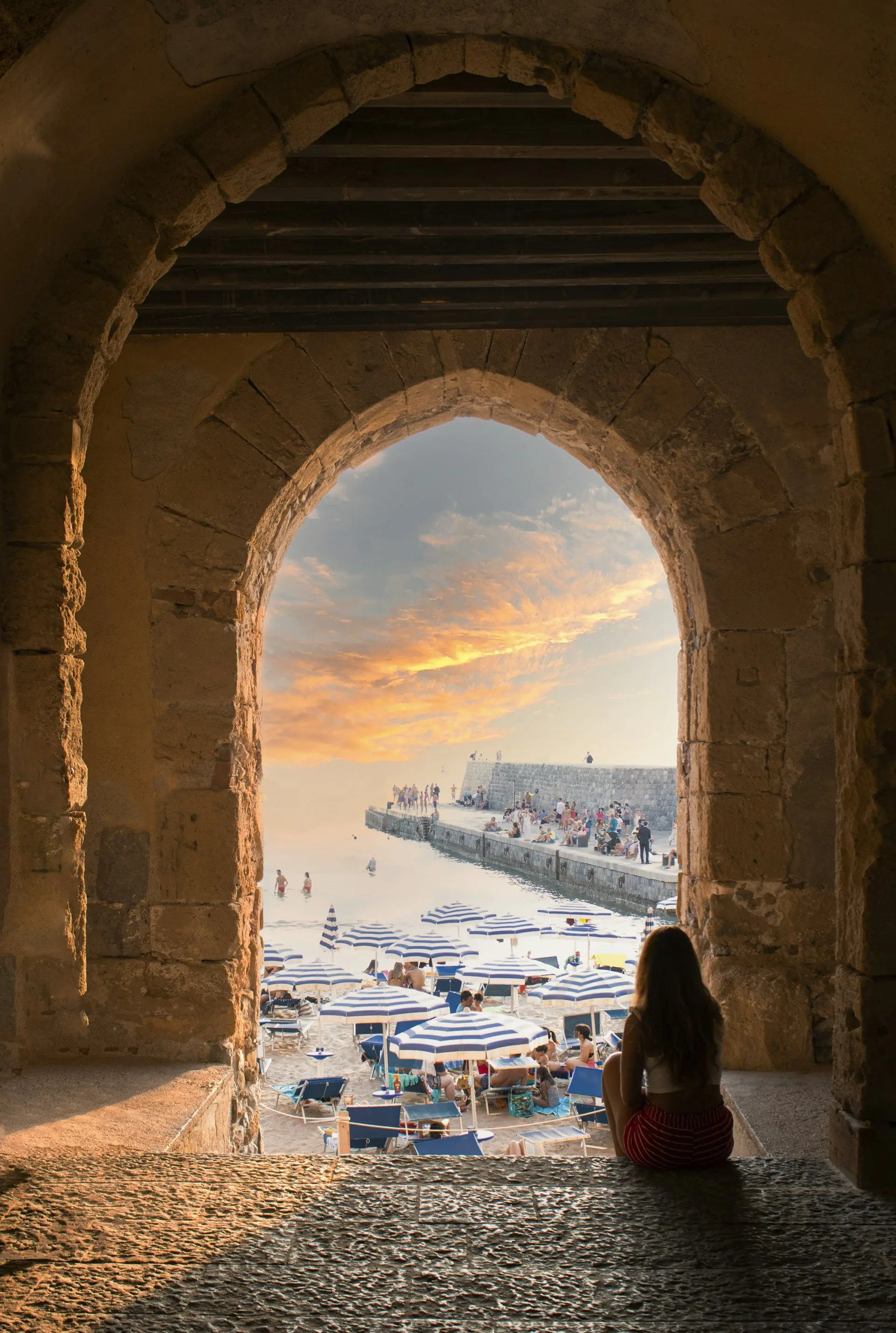 La playa de Cefalù al atardecer a través de un arco del paseo marítimo